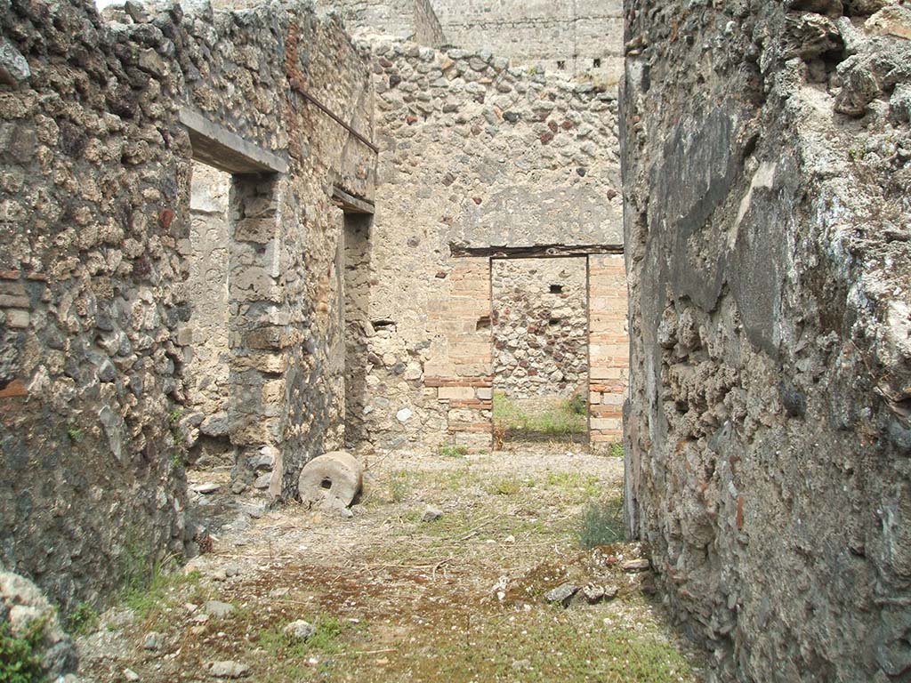V.2.g Pompeii. May 2005. 
Looking east through remains of site of doorway from room ‘o’, across room ‘p’ the portico, towards the doorway into room q, the triclinium.
The rear window/doorway of the tablinum is on the left, followed by the doorway to corridor ‘L’.
According to NdS, the portico was supported by pillars and columns. 
Under the portico was the doorway to room ‘q’ the triclinium which when found was quite rustic.
In the south wall, the triclinium had a large window onto the garden, which originally had been a doorway.
The small room ‘o’ had a window overlooking a room in the adjacent house (V.2.f, or V.2.B according to 1896 NdS plan on p.418).
Leaning against the wall outside the doorway to room ‘o’ was a masonry seat.
Encased in the same west wall was a slab of tufa with a phallus in high relief, in the middle of a niche with small pediment, and all painted in red with a yellow cornice.
This was most likely around the corner, on the right of this photo.
See Notizie degli Scavi di Antichità, 1896, (p.421).

