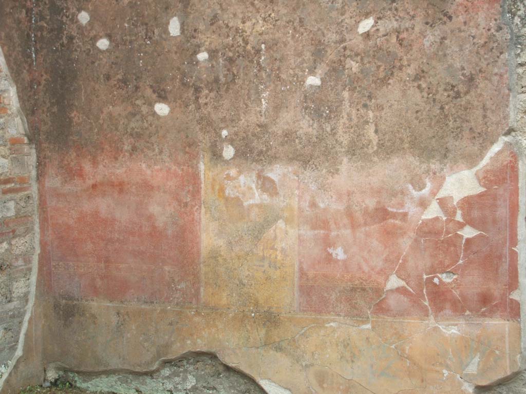 V.3.9 Pompeii. May 2005. West wall of site of room on the south side.
According to NdS, the south wall, on the left of the photo, was also divided into three panels.
The two side panels were red with a griffin and a flying tiger in gold.
The central panel was yellow and showed a painted closed door, framed by red and white pilasters with entablature.
In the middle was a painted door-knocker in the shape of an ox’s head.
Above this area, around the window that opened towards house V.3.8, there were other subtle architectural decorations in yellow on a red background.
Painted dolphins and other ornaments could be seen.
See Notizie degli Scavi di Antichità, 1902, dated November 1901, p.201-203.
