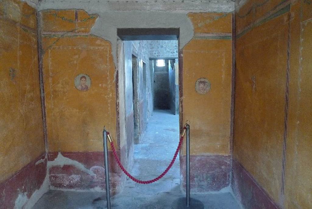 V.4.a Pompeii. July 2010. Room ‘i’, west wall of cubiculum, with doorway to atrium. 
On the walls are portrait medallions, one of a young girl and one of a boy with the attributes of Mercury (winged helmet and caduceus).
A large painting is of Pero suckling her father Micone and has a Latin inscription in white letters in the top left corner.
Photo courtesy of Michael Binns.
