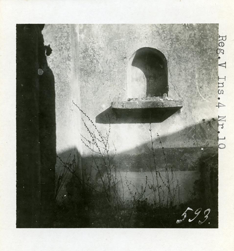 V.4.c Pompeii but shown as V.4.10 on photo, 1937 or earlier, by Tatiana Warscher. Niche lararium (e) in east wall of garden K.
Photo courtesy of American Academy in Rome, Photographic Archive. Warsher collection no. 593.
According to Boyce, this niche was placed at the east end of the corridor leading from the atrium.
The arched niche had a heavy ledge projecting from the wall. 
Upon this ledge was placed an ordinary roof tile, the raised edges of which, when covered with stucco would look like an altar.
The rear wall was painted blue or green, and painted with plants.
Boyce was not sure if this was a Lararium, but he thought as there was no other Lararium in the house, it may possibly have been one.
He said that Sogliano attached religious importance to a painting of Mercury found on the east wall of the atrium. 
See Notizie degli Scavi di Antichità, 1905, p. 131.
See Boyce G. K., 1937. Corpus of the Lararia of Pompeii. Rome: MAAR 14. (p.42, no.130, Pl. 3,1 - which is this photo by Warscher)
In a note on page 42, Boyce added that a collection of items were found, perhaps, gathered together for flight.
Included were a glazed terracotta statuette of Harpocrates and a small terracotta altar.
See Bullettino dell’Instituto di Corrispondenza Archeologica (DAIR), xvi, 1901, 364.

