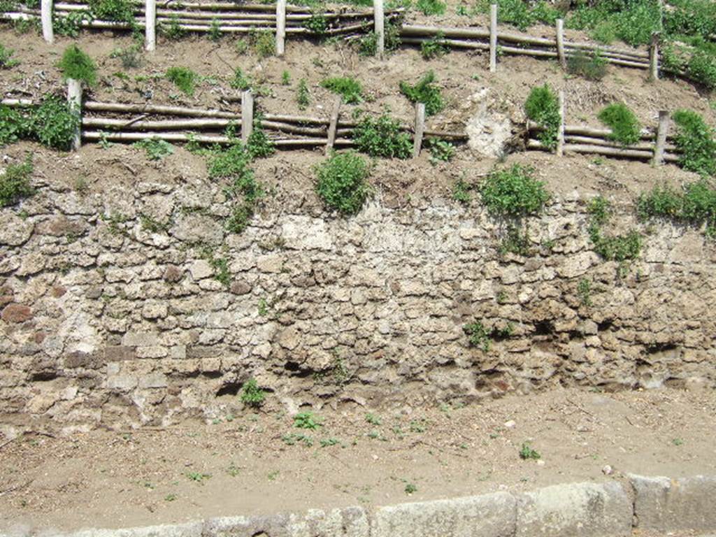 V.6.7 Pompeii. May 2006. Unexcavated façade/boundary wall.
The upper part of the rear of the unexcavated fountain / nymphaeum can be seen above the boundary wall, right of centre.
