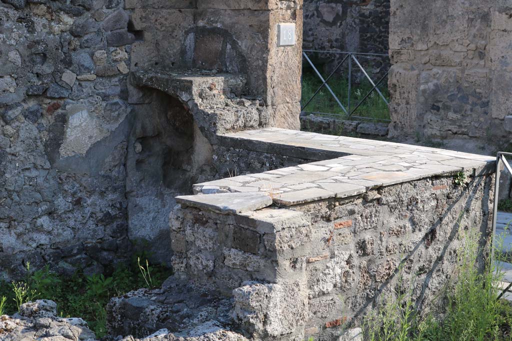 VI.1.18, Pompeii. December 2018. 
Looking south-west across hearth at east end of two-sided marble counter and two-tier shelving. Photo courtesy of Aude Durand.
