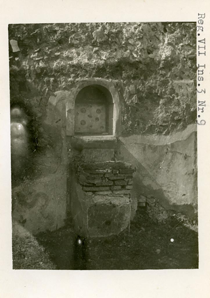 VII.3.8 Pompeii but shown as VII.3.9 on photo. 
1930s photo by Tatiana Warscher. Room “c”, west wall. Lararium and altar.
Photo courtesy of American Academy in Rome, Photographic Archive. Warsher collection no. 587.
According to Boyce –
“Against the W. wall of the central room of the dwelling quarters stands a masonry altar (0.45 by 0.50, h. 0.75), coated with yellow stucco and having the two serpents painted on the wall, one on each side of it. In the wall above the altar is an arched niche (h. 0.54, w. 0,47, d. 0.17, b. above the floor 1.0), its inside walls coated with red stucco, upon which the attributes of Hercules - a club and a skyphos twined with laurel - are reported to have been painted. The niche today shows a coating with white stucco bordered with red stripes, and upon it are painted realistic red roses. On the wall above the niche was the ordinary lararium painting of the Genius in white toga with cornucopia and patera and on each side of him a Lar. The background was richly decorated throughout: in the upper panel beside the Lares were plants and birds, on the interior of the niche were red roses, around the serpents were plants and flowers. A small panel between the top of the altar and the ledge projecting below the niche was painted in imitation of coloured marble.
Fiorelli states in the Scavi that the niche perhaps contained a statuette of Hercules, in the Descr. that it did contain such a statuette; the report in the Bull. Inst. mentions no statuette.
See Boyce G. K., 1937. Corpus of the Lararia of Pompeii. Rome: MAAR 14. (p.63-4, Pl.12,1). 



