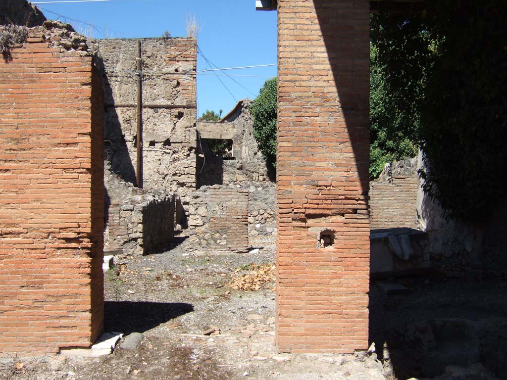 VII.4.25 Pompeii. September 2005. Doorways from VII.4.24 and VII.4.25 to rear rooms.
According to Boyce, on the west wall of the kitchen above the hearth, was a Lararium painting in two zones on a white background.
It showed the Genius pouring a libation upon an altar. On each side of him was a Lar in a blue tunic and red pallium.
Instead of the customary serpents, the lower zone was filled with a second sacrificial scene, but only the popa remains.
He held a knife in his right hand and held a hog with his left.
The hog was adorned with a red band around its belly and a garland.
See Boyce G. K., 1937. Corpus of the Lararia of Pompeii. Rome: MAAR 14.(p.65, no.272)
According to Garcia y Garcia, all the rear parts of this dwelling were damaged by the bombing in September 1943.
Demolition of the atrium, fauces and two other rooms in this area occurred, including the falling of the painted fourth style plaster.
See Garcia y Garcia, L., 2006. Danni di guerra a Pompei. Rome: L’Erma di Bretschneider. (p. 97)
According to Fröhlich, only slight faded traces of the lararium painting remain.
See Fröhlich, T., 1991. Lararien und Fassadenbilder in den Vesuvstädten. Mainz: von Zabern. (p.286, L84)
