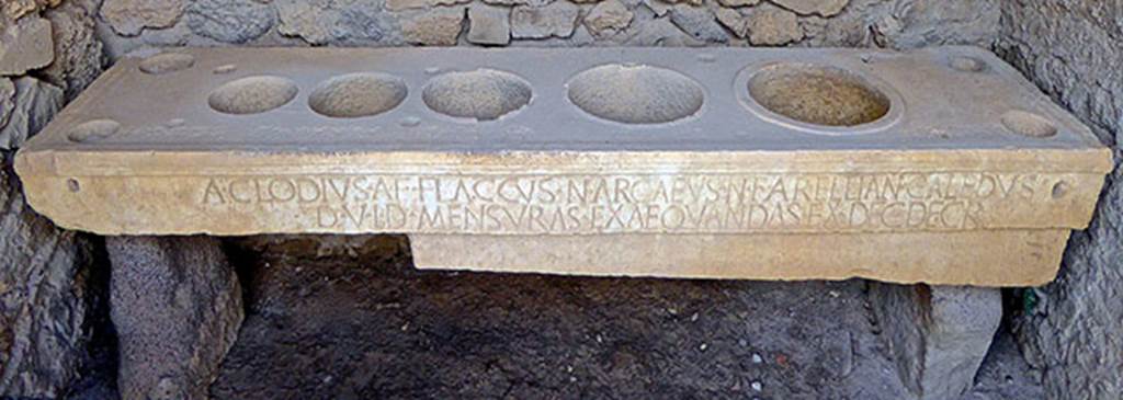 VII.7.31 Pompeii. September 2016. Mensa Ponderaria, with inscription on the front.
Photo courtesy of Michael Binns.
Original now kept in Naples Archaeological Museum. Inventory number 3828.

According to Epigraphik-Datenbank Clauss/Slaby (See www.manfredclauss.de), it read –

A(ulus) Clodius A(uli) f(ilius) Flaccus N(umerius) Arcaeus N(umeri) f(ilius) Arellian(us) Caledus
d(uum)v(iri) i(ure) d(icundo) mensuras exaequandas ex dec(urionum) decr(eto)      [CIL X 793]

According to Cooley this translates as:
Aulus Clodius Flaccus, son of Aulus, and Numerius Arcaeus Arellianus Caledus, son of Numerius, duumvirs with judicial power, saw to the standardization of the measures in accordance with a decree of the town councillors.
See Cooley, A. and M.G.L., 2004. Pompeii: A Sourcebook. London: Routledge, H64b, p. 179.
