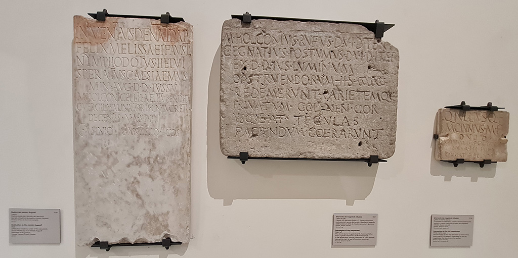 VII.7.32 Pompeii. 
On left: Dedication to Ministri Augustali, on display in “Campania Romana” gallery in Naples Archaeological Museum, inv.3783. 
Temple of Apollo (but then believed to be the Temple of Venus) (1 Marzo 1823) -

Inventus Dentat(ius) Daph(nus)
Felix Melissaei(!) Faust(us)
Nymphodotus Helvi(us)
Speratus Caesiae Mus(ae)
min(istri) Aug(usti) d(ecreto) d(ecurionum) iussu
M(arci) Holconi Gelli L(uci) Aeli Tuber(onis) d(uumvirorum) i(ure) d(icundo)
C(ai) Vergili Salinatoris Cn(aei) Lucreti
Decentis
[d(uum)vir(orum)] v(iis) a(edibus) s(acris) p(ublicis) p(rocurandis)
C(aio) Asinio C(aio) Antistio co(n)s(ulibus)      [CIL X, 895]

In the centre, on display in “Campania Romana” gallery in Naples Archaeological Museum, inv.3827.
Temple of Apollo (8 marzo 1817) -

M(arcus) Holconius Rufus d(uum)v(ir) i(ure) d(icundo) tert(ium)
C(aius) Egnatius Postumus d(uum)v(ir) i(ure) d(icundo) iter(um)
ex d(ecreto) d(ecurionum) ius luminum
opstruendorum(!) HS |(mille) |(mille) |(mille)
redemerunt parietemque
privatum col(onia) Ven(eria) Cor(nelia)
usque a<d=T> tegulas
faciundum coera(ve)runt      [CIL X. 787]

On right:
Temple of Apollo, from the room to the north of the portico, also called “sagrestia o cella del sacerdote “ (4 Aprile 1817) , inv. 3763.

Q(uintus) Tullius Q(uinti) f(ilius)
M(arcus) Cinnius M(arci) f(ilius)
d(uum)v(iri) i(ure) d(icundo)
C(aius) Mammius L(uci) f(ilius) C(aius) Naevius M(arci) f(ilius)
d(uum)v(iri) v(iis) a(edibus) s(acris) p(ublicis) p(rocurandis) ex d(ecreto) d(ecurionum)
constat HS DCLXXII s(emis)       [CIL X, 803]

