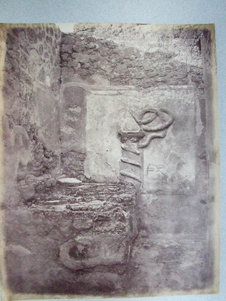 VII.15.13 Pompeii.  Kitchen with altar and Genius Lar relief on east wall.
Old undated photograph courtesy of the Society of Antiquaries, Fox Collection. A Lar can be made out in the top left hand corner, and a hog’s head on the right side of the altar.
