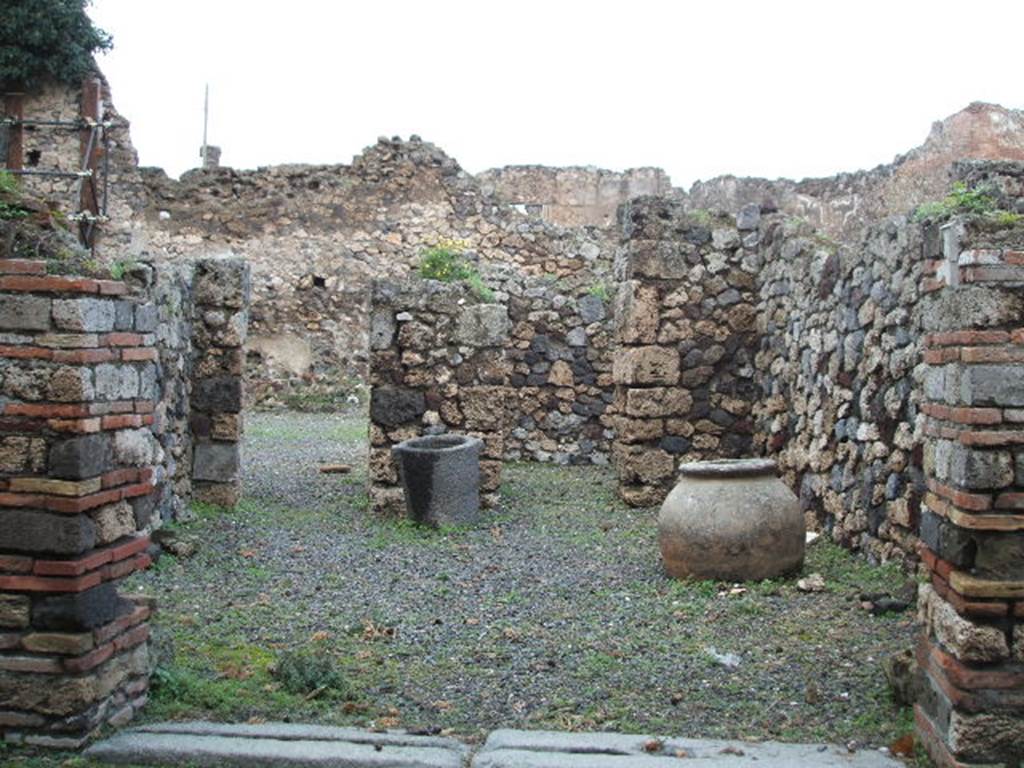 VII.16.4 Pompeii. December 2004. Looking north across shop towards doorway to atrium of VII.16.3, and doorway to rear room. On the left, in the west wall was another doorway to the entrance corridor of VII.16.3.  According to Boyce, in the east wall was a semicircular niche – la nicchia dei Penati, according to Fiorelli. 
See Boyce G. K., 1937. Corpus of the Lararia of Pompeii. Rome: MAAR 14. (p.73, no.336) 
According to Garcia y Garcia, this workshop was destroyed by the bombing of 13th September 1943, and then partially restored in 1950.
There is now no trace of a window at the rear looking into the atrium, as it has been replaced by a doorway.
The niche that Boyce described as being in the east wall, although there was doubt as to its exact position, has not been replaced at all. Avellino located it in the west wall, whereas Boyce said in the east wall.
See Garcia y Garcia, L., 2006. Danni di guerra a Pompei. Rome: L’Erma di Bretschneider. (p.131)
