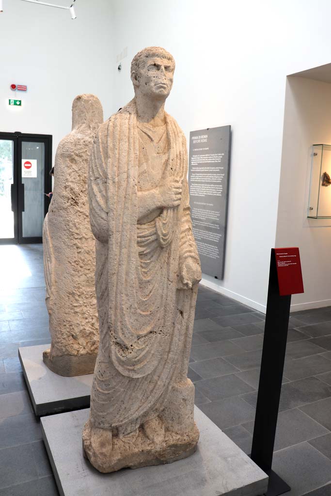 Porta Nocera tombs 34aEN. February 2021. 
Limestone funerary statue of a man wearing a toga, on display in Antiquarium.
Photo courtesy of Fabien Bièvre-Perrin (CC BY-NC-SA).
