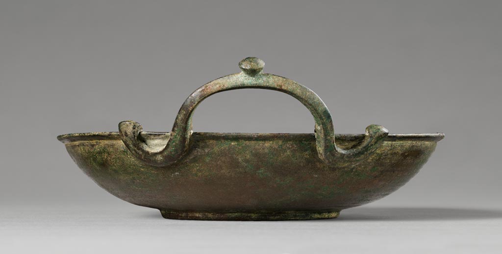 Discovered in a villa in Boscoreale. Shallow bronze patera bowl with single serpentine handle.
Digital image courtesy of the Getty's Open Content Program. Now in the Getty Museum, inventory number 72.AC.140.
This patera (shallow bowl) is undecorated except for a single serpentine handle with a knob at either end and one placed centrally on the raised part of the handle. Vessels of this type were used in the home for religious rituals and to hold water for handwashing during banquets. Slaves would pour water from an oinochoe (pitcher) over the hands of participants, catching the cascade in a patera held underneath. This patera was discovered in a villa at Boscoreale or in the vicinity, although the exact findspot is unknown. 
