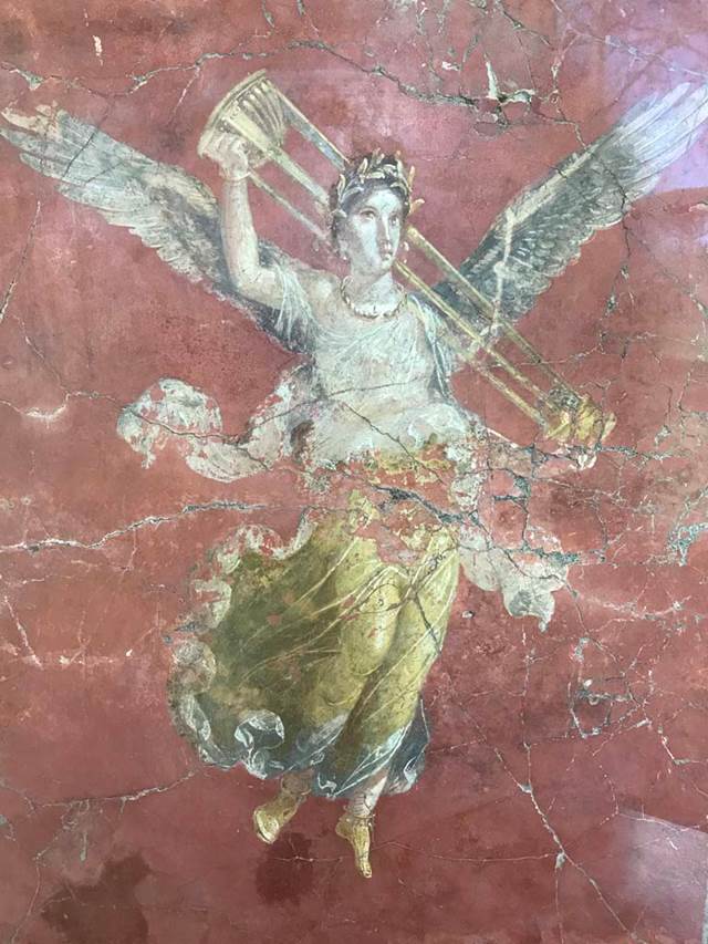 Complesso dei triclini in località Moregine a Pompei. April 2019. Triclinium C, east wall.
Vittoria con tripode. Vittoria with tripod, on display in Pompeii Palaestra.
Vittoria alata con gli attributi di Apollo. Winged Victory with the attributes of Apollo.
This is shown on the east wall of triclinium C but may have come from Triclinium D or E.
According to Mario Pagano, the difference in the background colour, red in this case, [triclinium D has black background colour] gives rise to the suspicion that this Winged Victory does not belong, as shown by the confused documentation, to the destination of triclinium D, but to that of the adjacent triclinium [E?], of which there is no recovery of the pictorial decoration.
See Guzzo, P., (A Cura di), 1997. Pompeii: Picta Fragmenta. Torino: Umberto Allemandi, p. 149 no. 116.
Photo courtesy of Rick Bauer.
