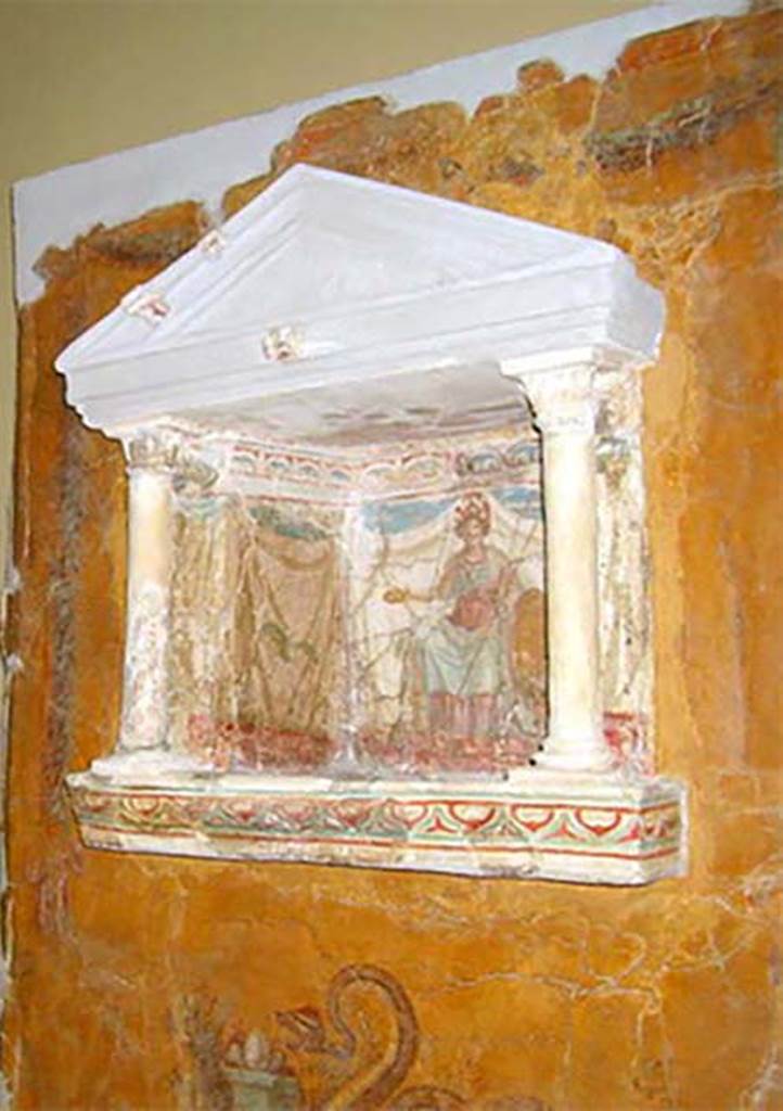 Gragnano, Villa rustica in Località Carmiano, Villa A. Lararium niche. 
From dividing pilaster between kitchen room 4 and room 2. 
Lararium in stucco found inserted in a yellow painted wall.
The lararium had a triangular pediment supported by two Corinthian columns.
The painting at the rear showed an enthroned Minerva with breastplate, helmet, shield, lance in the left hand and gilded/golden plate in the right. 
