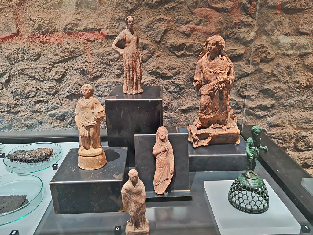 II.1.12 Pompeii, March 2024. Photo courtesy of Giuseppe Ciaramella.
No. 1 (on right) – Statuette of boy in short tunic (perfume burner ?), Bronze, Ist century AD.
(No. 1 – Statuetta di fanciullo in tunica corta (bruciaprofumi?), Bronzo, I sec. d.C.)
On display in exhibition in Palaestra, entitled - “L’altra Pompei, vite comuni all’ombra del Vesuvio”. 
